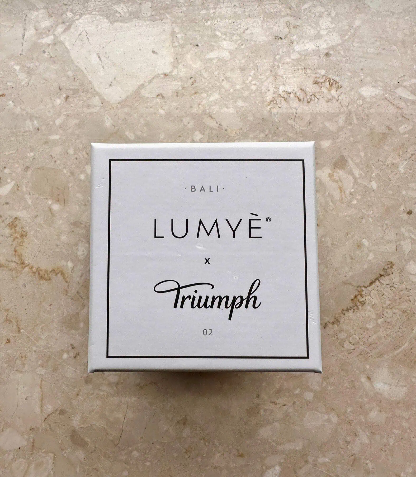 Pudełko Lumyè x Triumph na marmurowym tle.